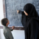Image: Boy standing at a black board being taught by teacher at a school in Yemen